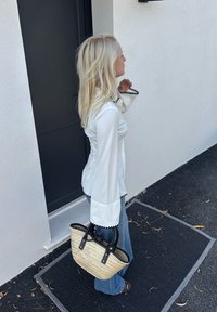 Biela blúzka s rukávmi v tvare zvona, čiernym lemovaním a priliehavým pásom. Džínsy so širokými nohavicami. Woven taška zo slamy s čiernymi uchami.