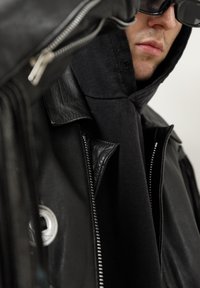 Veste en cuir noir avec fermetures éclair argentées et grand col, portée sur un sweat à capuche noir. Texture lisse avec une coupe ajustée.