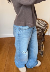 Ljust blå slitna jeans med vid bendesign, med synlig fransning, i kombination med beige skor och en texturerad brun tröja.