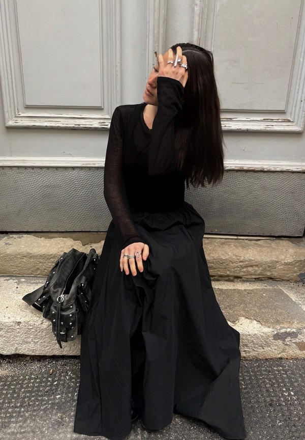 Black long-sleeve top and a flowing black skirt made from a lightweight fabric. Accessories include several silver rings and a studded black handbag.
