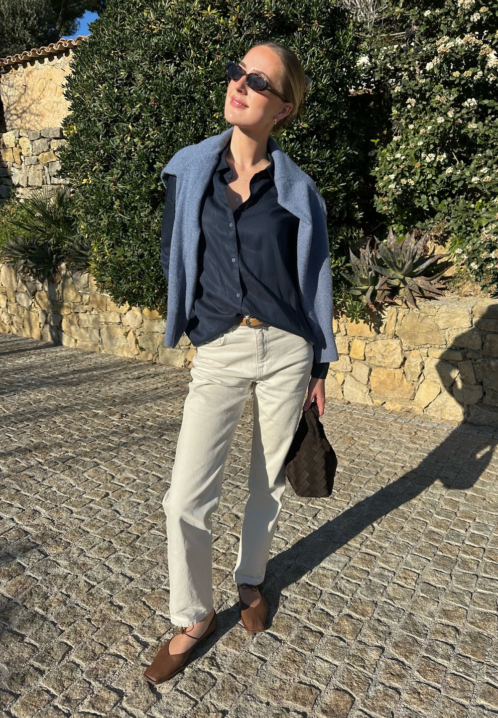 Το μοντέλο φορά μια ναυτική πουκάμισο με κουμπιά, μπεζ παντελόνια και καφέ επίπεδα παπούτσια. Μια ανοιχτού μπλε κάπα είνα�ι ριγμένη στους ώμους της. Κρατά μια σκούρα πλεκτή τσάντα.