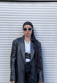 Czarny, oversize'owy skórzany blezer z białym t-shirtem i czarnym paskiem. Dodatki to złote łańcuchy, czarna chusta na głowę oraz białe okulary przeciwsłoneczne w stylu cat-eye.