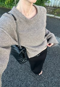 Světlé hnědé, texturované svetr s širokým výstřihem, spárovaný s černou, prošívanou kabelkou a přiléhavou černou sukní.