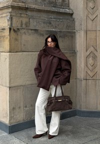 Oblečen velik rjav volnen plašč s pripadajočo rjavo ruto, kombiniran z belimi zvončastimi hlačami in temno rjavo semiš torbico. Rjavi koničasti škornji s peto.