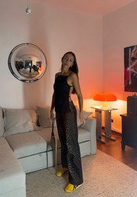 Black sleeveless top, leopard print wide-leg trousers, and yellow trainers. A round mirror reflects the room with an orange lamp and beige sofa.