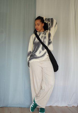 Jersey crema de gran tamaño con estampado de tie-dye negro, combinado con pantalones beige de pierna ancha y zapatillas verdes. Bolso trenzado negro cruzado al cuerpo.