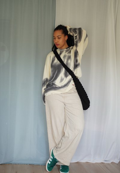 Jersey crema de gran tamaño con estampado de tie-dye negro, combinado con pantalones beige de pierna ancha y zapatillas verdes. Bolso trenzado negro cruzado al cuerpo.