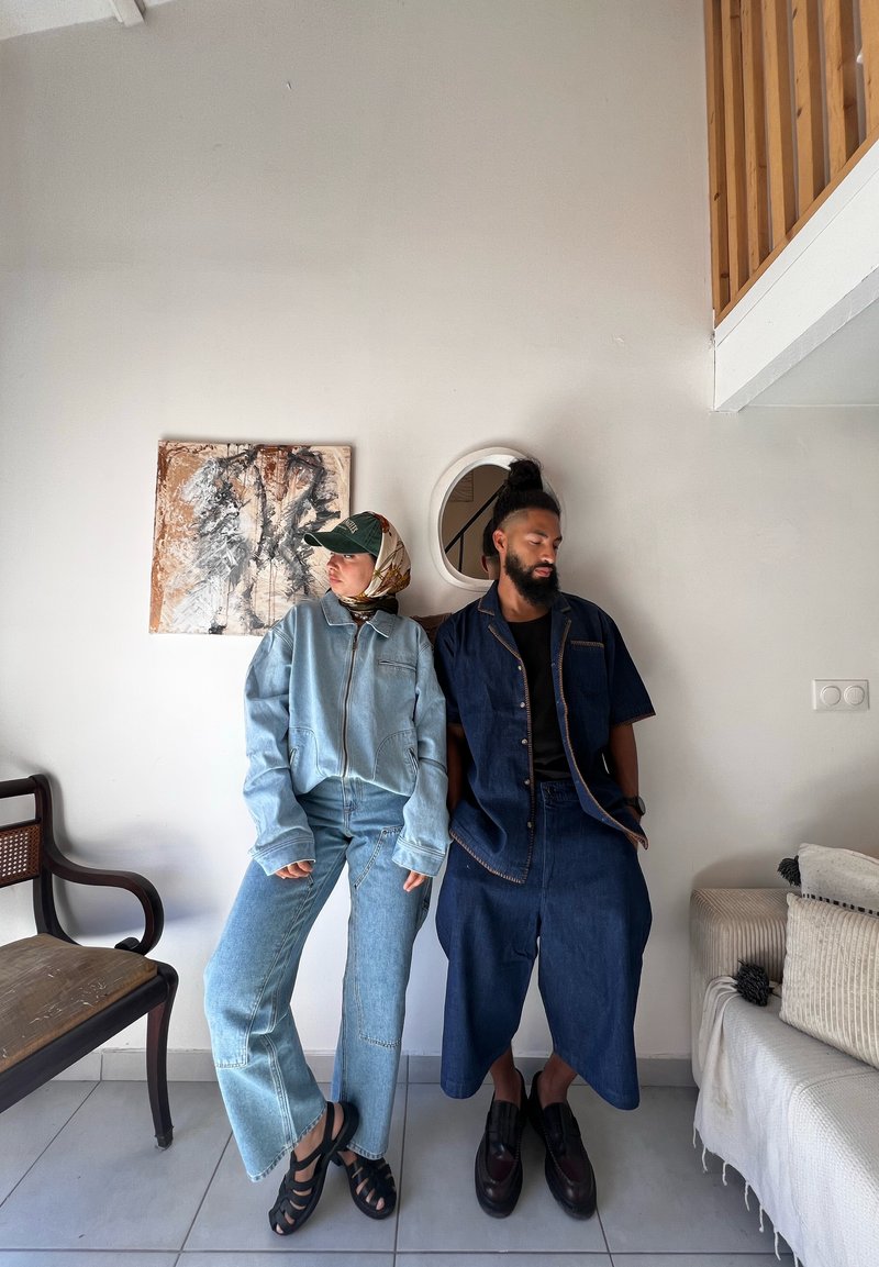 Giacca di denim azzurro chiaro e jeans su una persona, abbigliamento in denim scuro sull'altra, entrambi accompagnati da accessori testurizzati e un divano morbido.