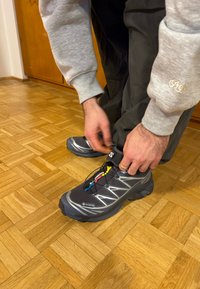 Chaussures de randonnée noires et grises avec tige en textile et semelle en caoutchouc, dotées d'un système de laçage rapide et d'un logo GORE-TEX ; fond de sol en bois dur.