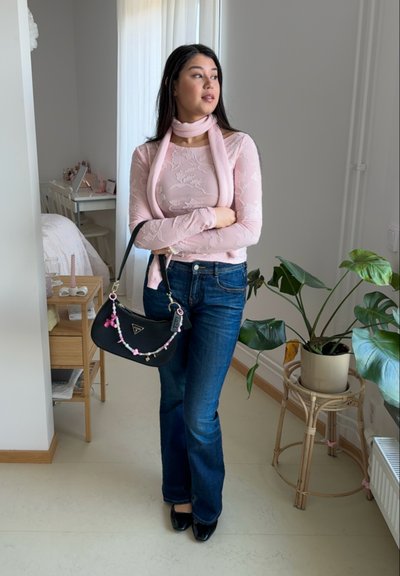 Top de manga larga texturizado rosa claro con bufanda a juego; jeans acampanados azul oscuro; bolso negro con charms decorativos; zapatos negros elegantes.