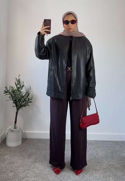 Chaqueta oversized de cuero negro, top negro, pantalones de pierna ancha morado oscuro, bolso rojo y zapatos de tacón rojos. Decoración minimalista en el fondo.