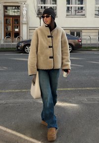 Casaco de lã beige com botões pretos, jeans de corte descontraído, botas de plataforma em tom bege, gorro preto e uma mala de ombro de cor clara.