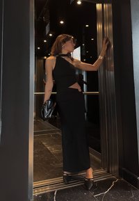 Melna, pieguļoša kleita ar vienu plecu un izgriezuma detaļu, kombinēta ar melnu rokassomiņu un augstpapēžu kurpēm. Mūsdienīgs un elegants dizains liftā.