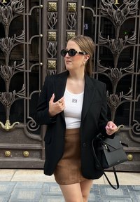 Μαύρο oversized σακάκι συνδυασμένο με λευκή ριγωτή μπλούζα και καφέ σουέτ μίνι φούστα. Αξεσουάρ περιλαμβάνουν μαύρα γυαλιά ηλίου και μια δομημένη τσάντα.