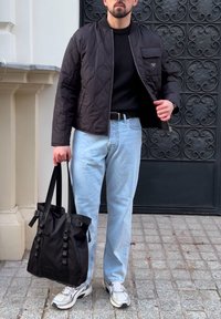 Černá prošívaná bomber bunda, černý svetr, světle modré džíny, stříbrné tenisky a černá taška tote s nastavitelnými popruhy. Texturovaný povrch.