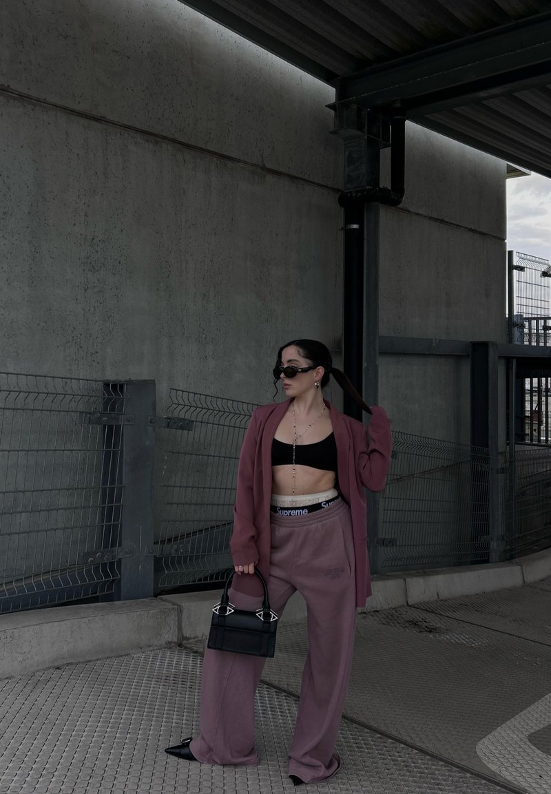 Υπερμεγέθης μωβ σακάκι πάνω από ένα μαύρο crop top, σε συνδυασμό με μωβ φόρμες και μια μικρή μαύρη τσάντα χειρός με μοναδικές λεπτομέρειες στα υλικά.