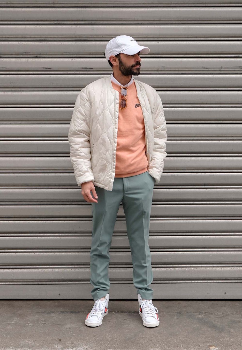 Quiltad krämfärgad bomberjacka, ljusorange tröja, mintgröna byxor och vita sneakers med röda detaljer, stående mot en grå bakgrund.