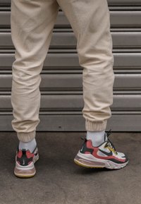 Zapatillas con un diseño multicolor que presentan acentos en blanco, negro, rojo y amarillo, combinadas con joggers de canalé en color crema y calcetines blancos.
