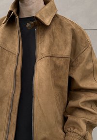 Brown suede jacket with a zip-front, snap-button collar, and elasticated cuffs. Features a relaxed fit and smooth texture.