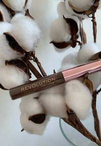 Produit Revolution Makeup London, tube marron avec des accents en or rose, entouré de boules de coton blanches sur un fond clair.