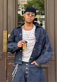 Denim jakna in usklajeni hlače v temnem pranju z srebrno kovino. Bela majica s tiskanjem besedila. Drži rjavo skodelico za kavo.