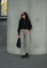 Μαύρο ζακέτα με φερμουάρ, παντελόνι λεοπάρ, μαύρες πλατφόρμες και μία μαύρη τσάντα. Στηρίζεται σε έναν τοίχο από σκυρόδεμα.