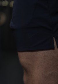 Close-up da coxa de uma pessoa a usar calções desportivos escuros da Nike, com um discreto logo swoosh visível perto da bainha.