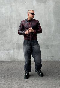 Giubbotto di pelle bordeaux con dettagli a costine, abbinato a jeans in denim scuri a vestibilità ampia con dettagli sulle cuciture. Stivali platform neri completano il look.