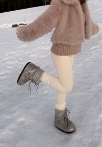 Bottes de neige étanches grises à finition texturée, semelles épaisses et lacets, associées à des leggings crème et une veste beige duveteuse.