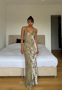 Robe satin vert olive avec un décolleté en V plongeant, coupe ajustée et une texture florale complexe. Bretelles spaghetti et design long jusqu'au sol.