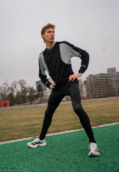 Top negro de manga larga con acentos grises, leggings negros y zapatillas deportivas blancas con rayas negras, en un campo de césped verde.