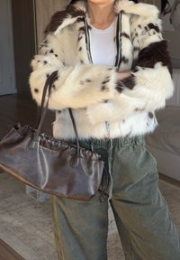 Faux fur-jacka i krämfärgad med bruna prickar, med dragkedja fram och huva. Matchas med en brun läderväska med rynkdetaljer.