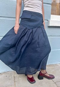 Σκούρο μπλε πλισέ φούστα από ελαφρύ ύφασμα, με στρωμένη σχεδίαση και υφή. Συνοδεύεται από μπορντό γόβες.