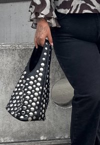 Sac bandoulière en cuir noir orné de larges clous argentés, de forme semi-ovale, à texture lisse, avec une large ouverture pour un accès facile.