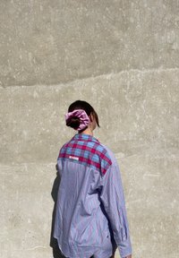 Prugasta košulja u plavoj i crvenoj boji s kariranim uzorkom na ramenu. Ima opušteni kroj i ušiveni natpis na gornjem dijelu leđa.