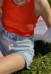 Imagem em primeiro plano de uma t-shirt laranja canelada combinada com calças de ganga azuis de cintura alta, apresentando um fecho de botão e uma barra dobrada.