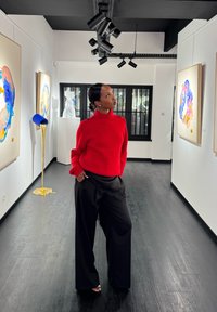 Czerwony prążkowany sweter z golfem i guzikami na ramionach, zestawiony z czarnymi szerokimi spodniami. Galeria z kolorową abstrakcyjną sztuką i wyjątkowym oświetleniem.