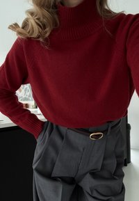 Roter Rollkragenpullover mit gerippter Textur; kombiniert mit hoch taillierter grauer Hose mit Falten; gesichert mit einem braunen Gürtel und goldener Schnalle.