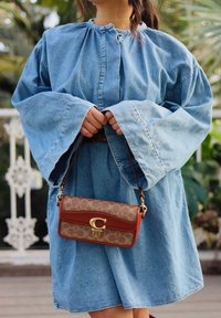 Robe en denim clair avec des manches larges et un col froncé, accompagnée d'un sac à main à motifs marron et beige avec un fermoir doré.