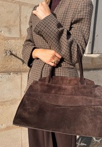 Braune Wildleder-Handtasche mit strukturierter Form, ausgestattet mit zwei kurzen Griffen und horizontalen Steppnähten. Kombiniert mit einem Hahnentrittmuster-Blazer.