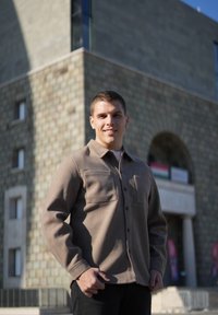 Barna, textúrált ing, két elülső zsebbel, gombos záródással és gallérral. Fehér ing fölött viselve, sötét nadrággal párosítva. Világos kültéri környezet.