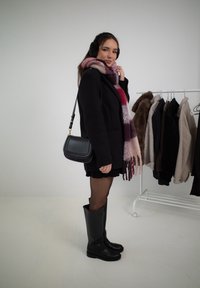 Musta takki, vaaleanpunais- ja purppuraraidallinen huivi, mustat minihame, mustat polvisukat saappaat ja pieni musta olkasalkku.