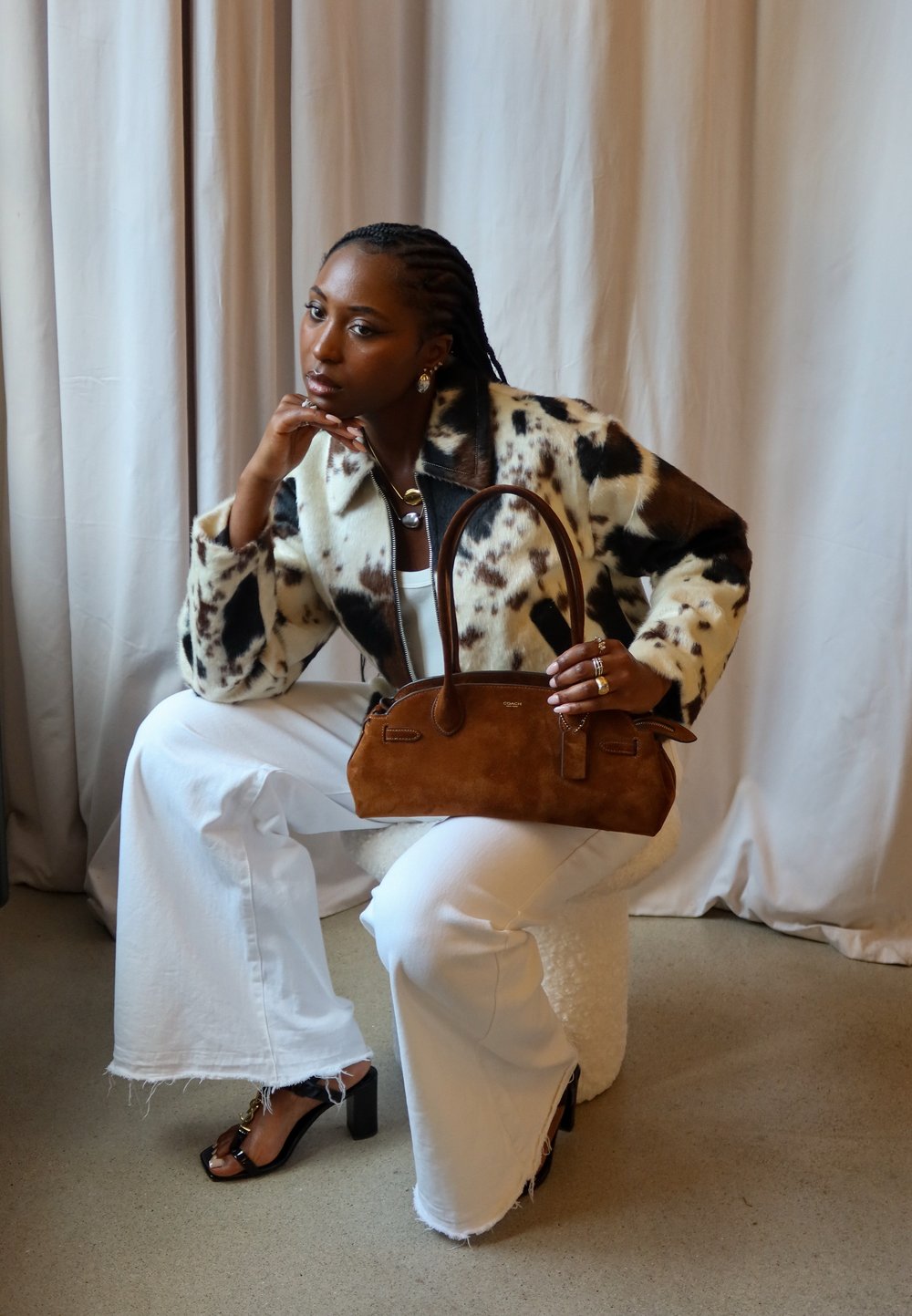 Brown suede handbag with leather handles, carried by a person in a spotted faux fur coat, teamed with white wide-leg trousers.