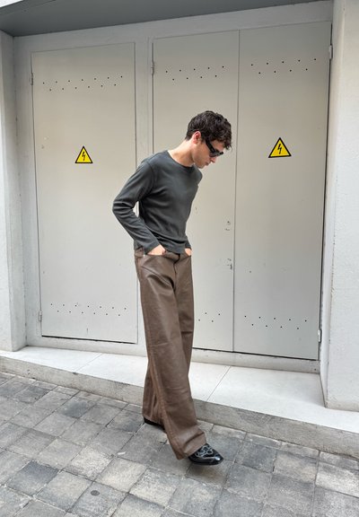 Camisa de manga larga verde oscuro, pantalones anchos de cuero marrón y zapatos negros. Diseño minimalista con bolsillos y texturas suaves.