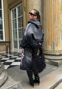 Hanorac negru supradimensionat cu dungi albe, fustă din denim cu grafică roz, geantă neagră de blană și cizme negre până la genunchi.