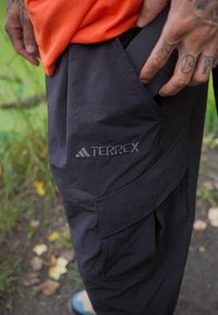 Zwarte Terrex-broek met een gestructureerde afwerking, voorzien van een grote zijzak en veredelde branding. Het materiaal lijkt lichtgewicht en duurzaam te zijn.