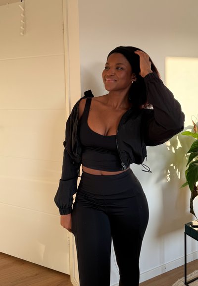 Chaqueta corta negra con puños elásticos, combinada con una camiseta negra sin mangas y leggings de cintura alta; diseño minimalista, textura suave.