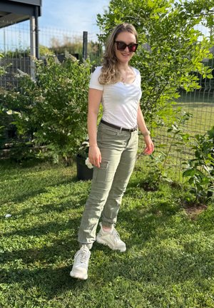 Camiseta blanca ajustada y ligera combinada con pantalones cargo verdes oliva que cuentan con bolsillos. Zapatillas deportivas con base blanca y detalles en rosa.