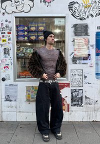 Long-sleeve, patterned grey shirt worn beneath a brown fur jacket, teamed with black wide-leg trousers and chunky black shoes featuring metallic accents.
