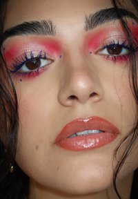 Nahaufnahme eines Gesichts mit pinkem Lidschatten, blauer Eyeliner und glänzenden nude Lippen, dazu braune Augen und definierte Augenbrauen in sanftem Licht.